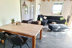 Ein modernes Wohnzimmer mit einem Holzesstisch, schwarzen Sofas und einem grauen, gemusterten Pouf.
