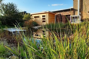 A rustic building with a wooden exterior, surrounded by tall grass and a small pond.