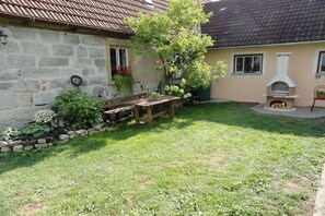 A stone house with a tiled roof, a wooden bench, a small garden with plants, and a wood-fired oven. - at the Albig holiday farm (Geslau)