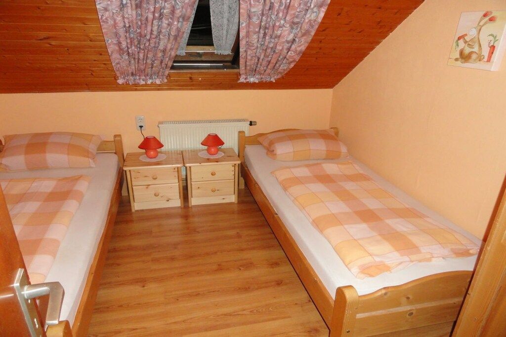 A small, cozy room with two wooden beds, each with a checkered bedspread. There are two bedside tables with lamps and a radiator above.