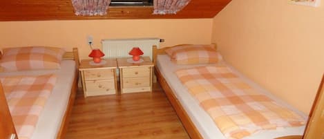 A small, cozy room with two wooden beds, each with a checkered bedspread. There are two bedside tables with lamps and a radiator above.