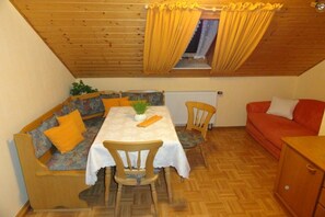 A cozy dining area with a wooden ceiling, a table with a white tablecloth, and a red sofa. - at the Albig holiday farm (Geslau)
