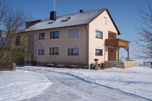Ein zweistöckiges Haus mit Balkon, Schornstein und einer verschneiten Einfahrt.