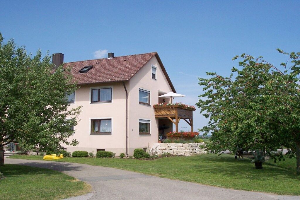 Ein zweistöckiges Haus mit einem geneigten Dach, einer Veranda und einer Steinmauer.