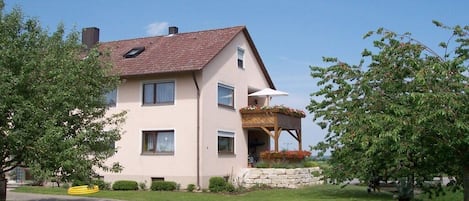 Ein zweistöckiges Haus mit einem geneigten Dach, einer Veranda und einer Steinmauer.