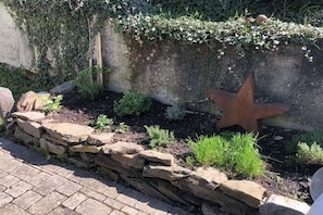 A garden with a stone wall, a star-shaped metal sculpture, and various plants. - Villa on Bleidenberg (Oberfell)