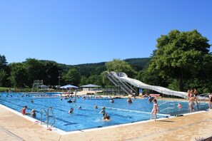Ein Schwimmbecken mit mehreren Bahnen, einer Wasserrutsche und einem Rettungsschwimmerstand.