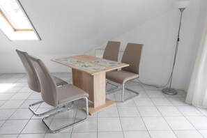 Un coin repas comprenant une table et quatre chaises, un lampadaire et une fenêtre avec des stores.