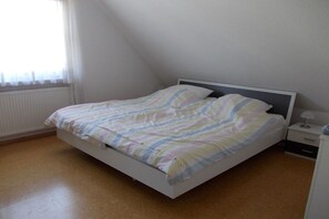 Ein Einzelbett mit gestreifter Bettdecke in einem Zimmer mit Heizkörper, Nachttisch und Lampe.
