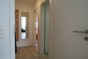 Un couloir avec une porte sur la droite, un miroir sur la gauche et un interrupteur sur le mur.