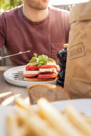Eine Person sitzt an einem Tisch mit einem Sandwich, einem Pfefferstreuer und einer Papiertüte.