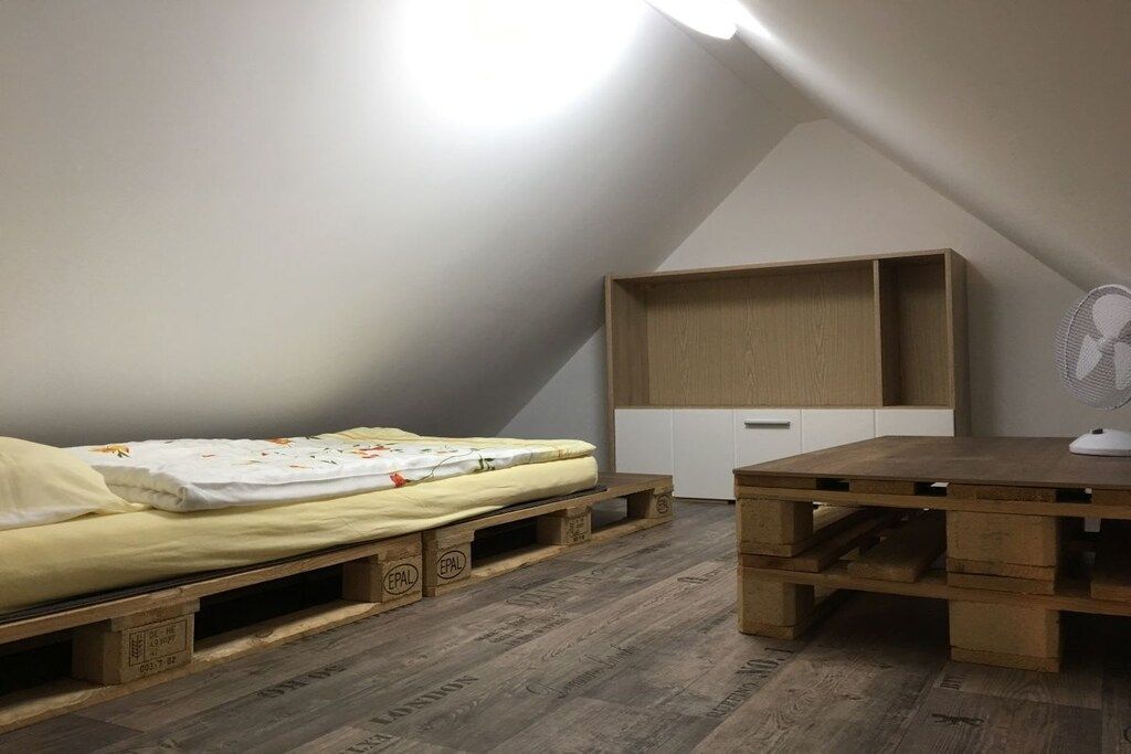 Eine kleine Einzimmerwohnung mit Schlafplatzart Hebebett, einem Holztisch und einer eingebauten Regaleinheit.