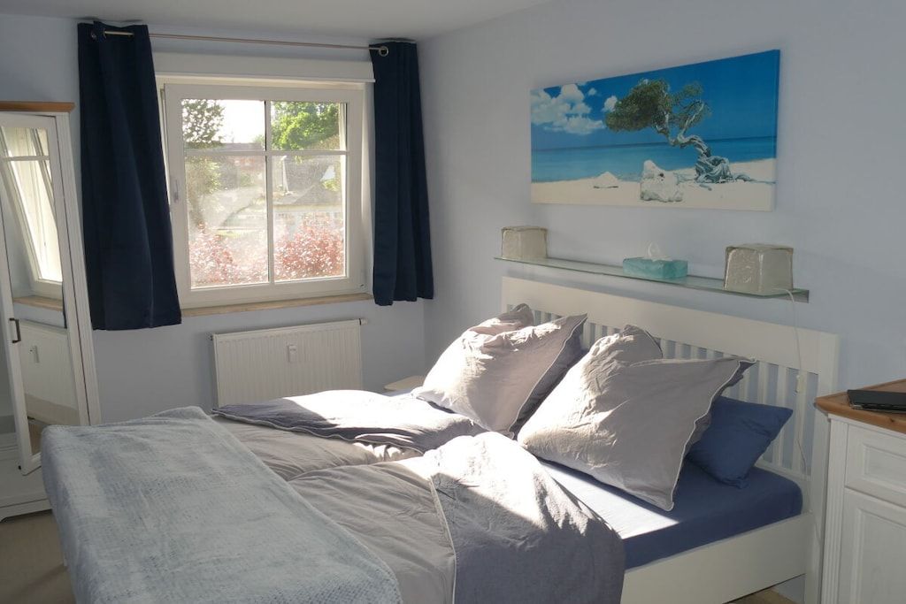 Une chambre à coucher avec un lit, une fenêtre avec des rideaux, un tableau au mur et une table de chevet.