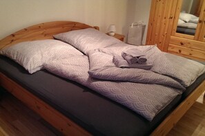 Ein Einzelbett mit Holz-Kopfteil, einer dunklen Matratze und gemusterten Kissen.