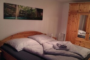 A bedroom with a wooden headboard, a bed with patterned bedding, a nightstand with a lamp, and a wooden wardrobe. - Holiday apartment on the Rhine and Moselle (Koblenz)