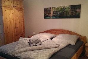 Ein Schlafzimmer mit einem hölzernen Bett, einem Kopfteil, einem Nachttisch, einem Holzschrank und einem an der Wand hängenden Gemälde.