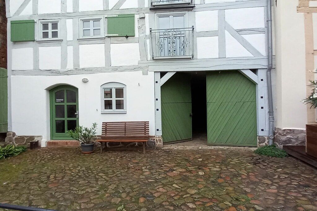 Ein traditionelles Fachwerkhäuschen mit grüner Tür, einer Bank und einem Blumentopf im Innenhof.