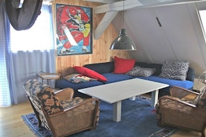 A cozy loft-style room with a blue sofa, wicker chairs, a white coffee table, and a large painting on the wall. - Holiday home in Tangermünde with Wi-Fi (Tangermünde)