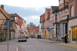 A cobblestone street lined with traditional half-timbered buildings, a clock tower in the distance, and a blue directional sign. - Holiday home in Tangermünde with Wi-Fi (Tangermünde)