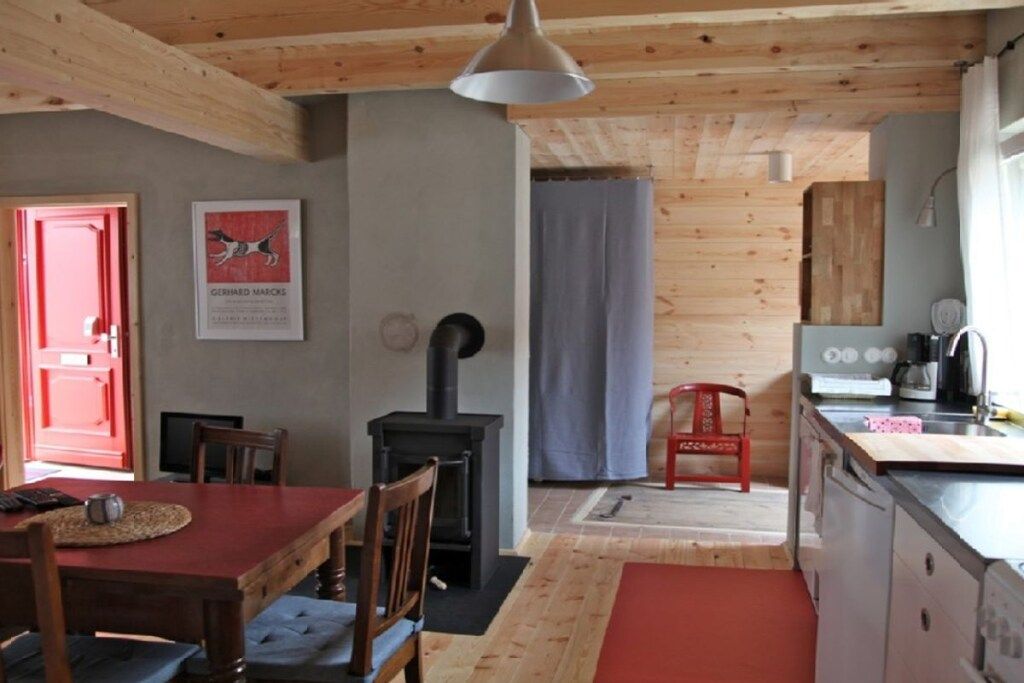 Une cuisine chaleureuse avec un poêle à bois, un coin repas avec une table rouge et une chaise rouge.