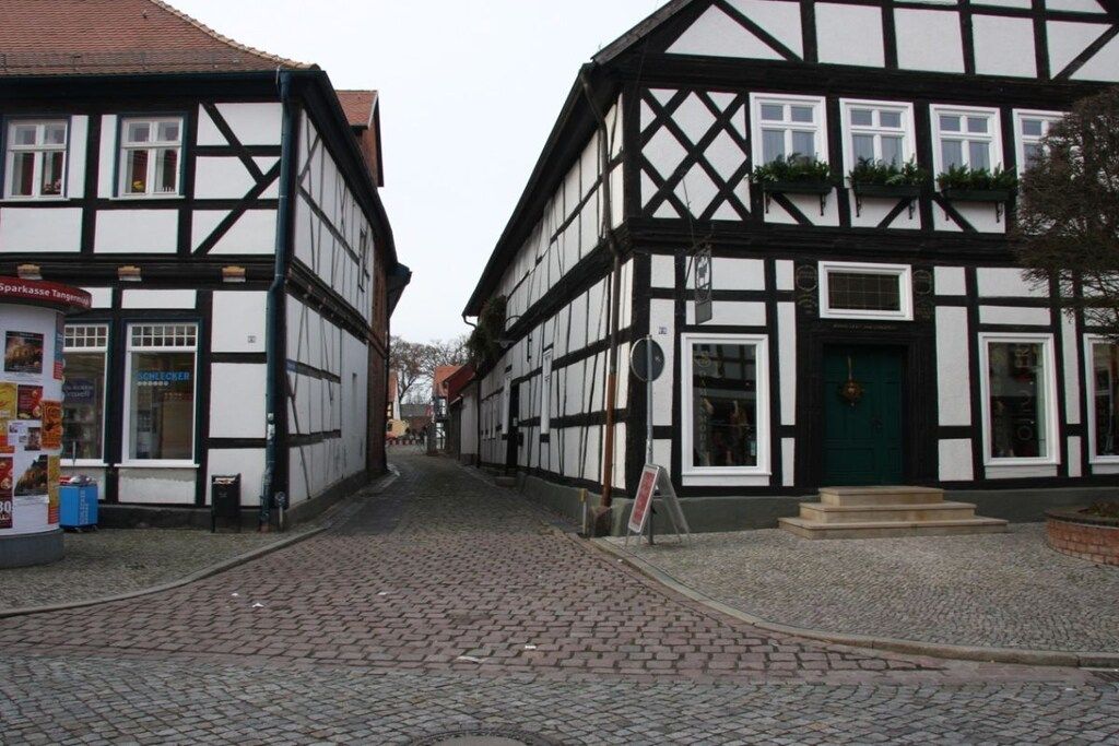 A narrow cobblestone street lined with traditional half-timbered buildings, one with a visible shop sign.
