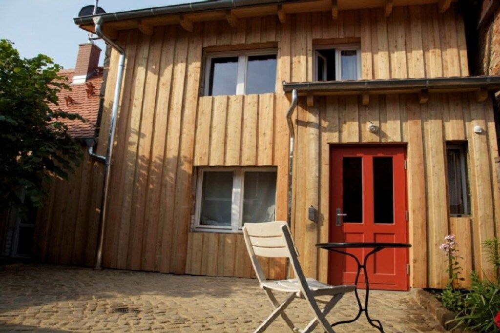 Un edificio de madera con puerta roja, una ventana y una silla afuera.