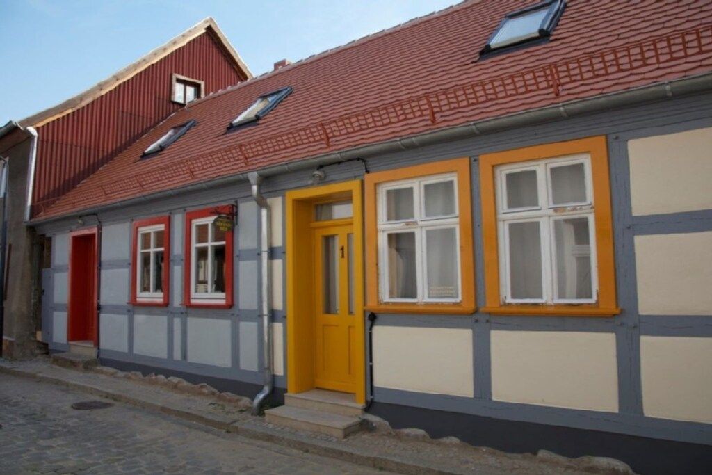 Une maison traditionnelle à colombages, avec un toit rouge, une porte jaune et des fenêtres à cadre blanc.