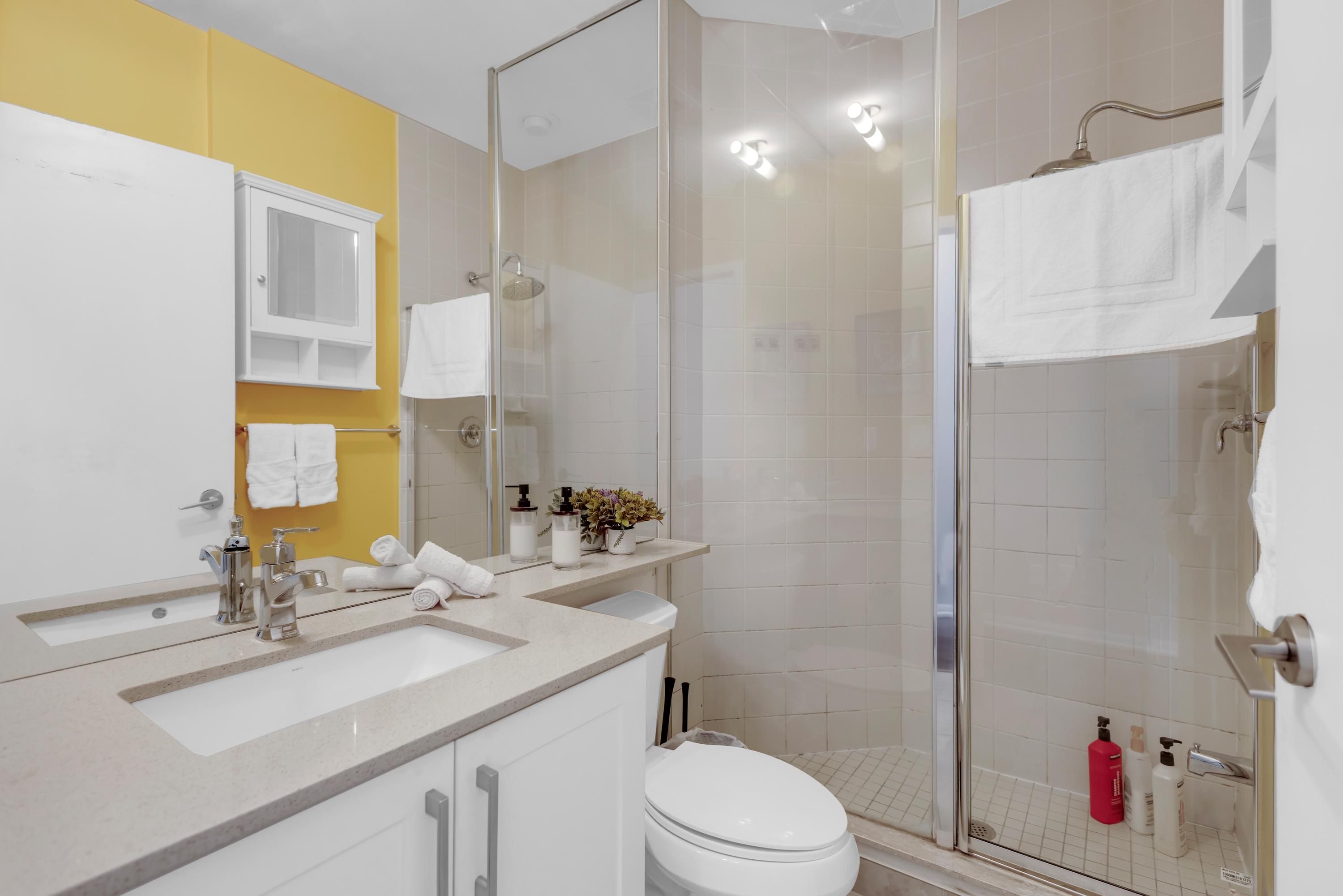 Un baño con cabina de ducha de vidrio, un lavamanos blanco y una pared de acento amarilla.