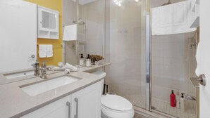A bathroom with a glass shower enclosure, a white sink, and a yellow accent wall. - StayToronto - Toronto Central Studio - DT (Toronto)