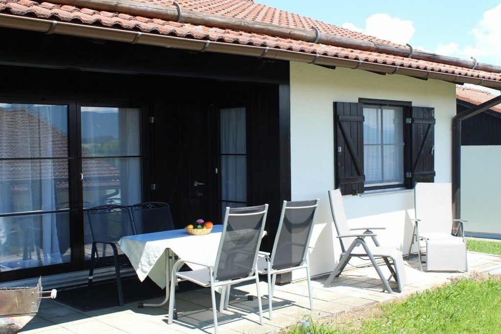 Eine überdachte Terrasse mit Tisch und Stühlen, ein Fenster mit Blick und ein Ziegeldach.