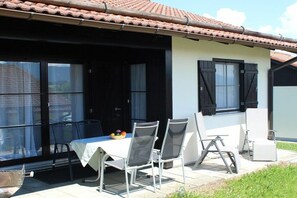 A covered patio with a table and chairs, a window with a view, and a tiled roof. - Holiday home "Säuling" (Lechbruck)