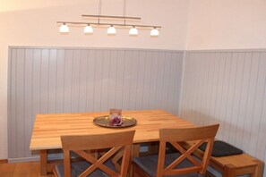 A dining area with a wooden table and chairs, a tray with a flower, and a pendant light fixture. - Holiday home "Säuling" (Lechbruck)
