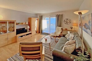 Ein modernes Wohnzimmer mit Sofa, Sesseln, Fernseher und einem Essbereich mit Schrank.