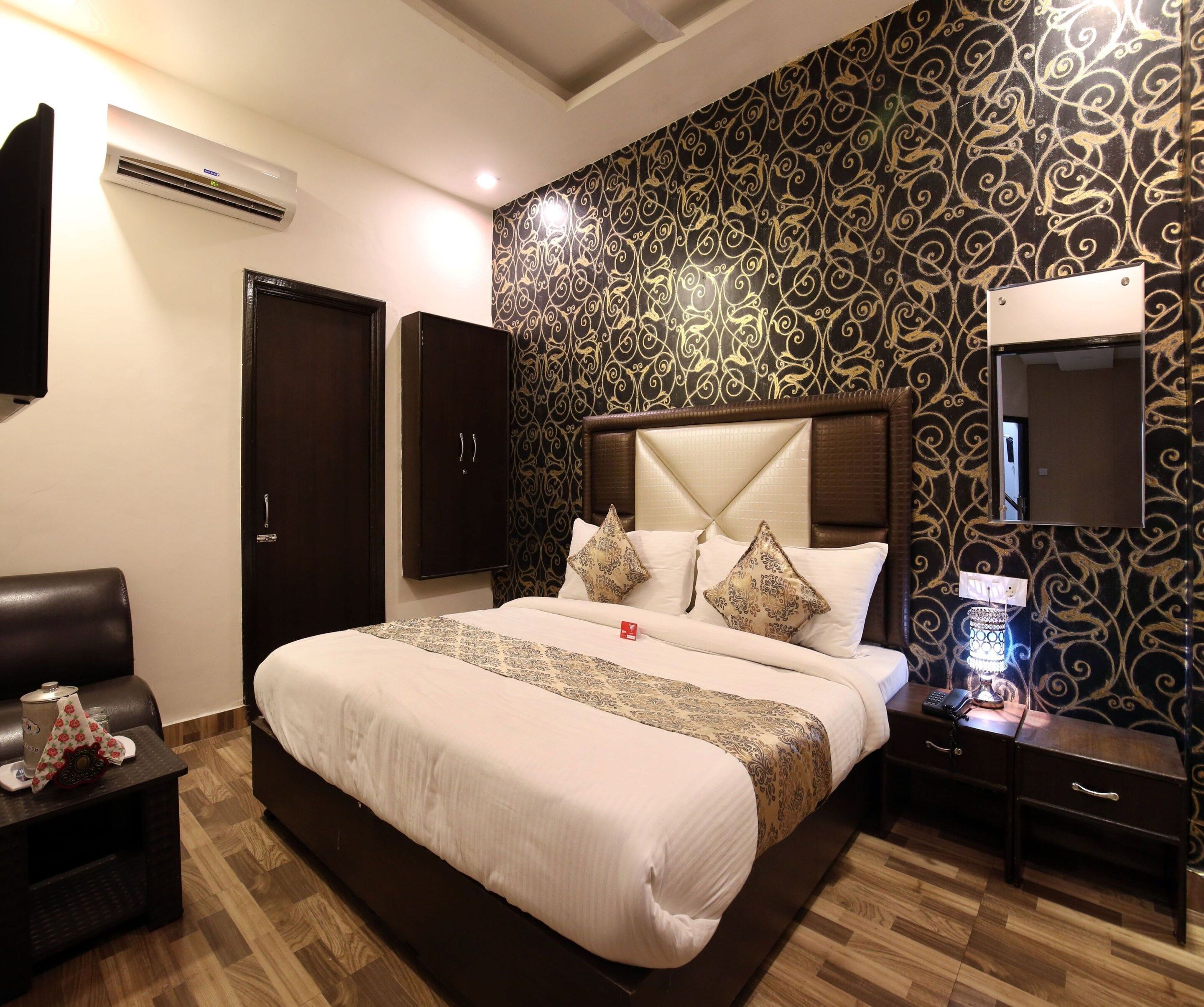 Quarto de hotel com uma cama grande, televisão, mesa de cabeceira com abajur e guarda-roupa.