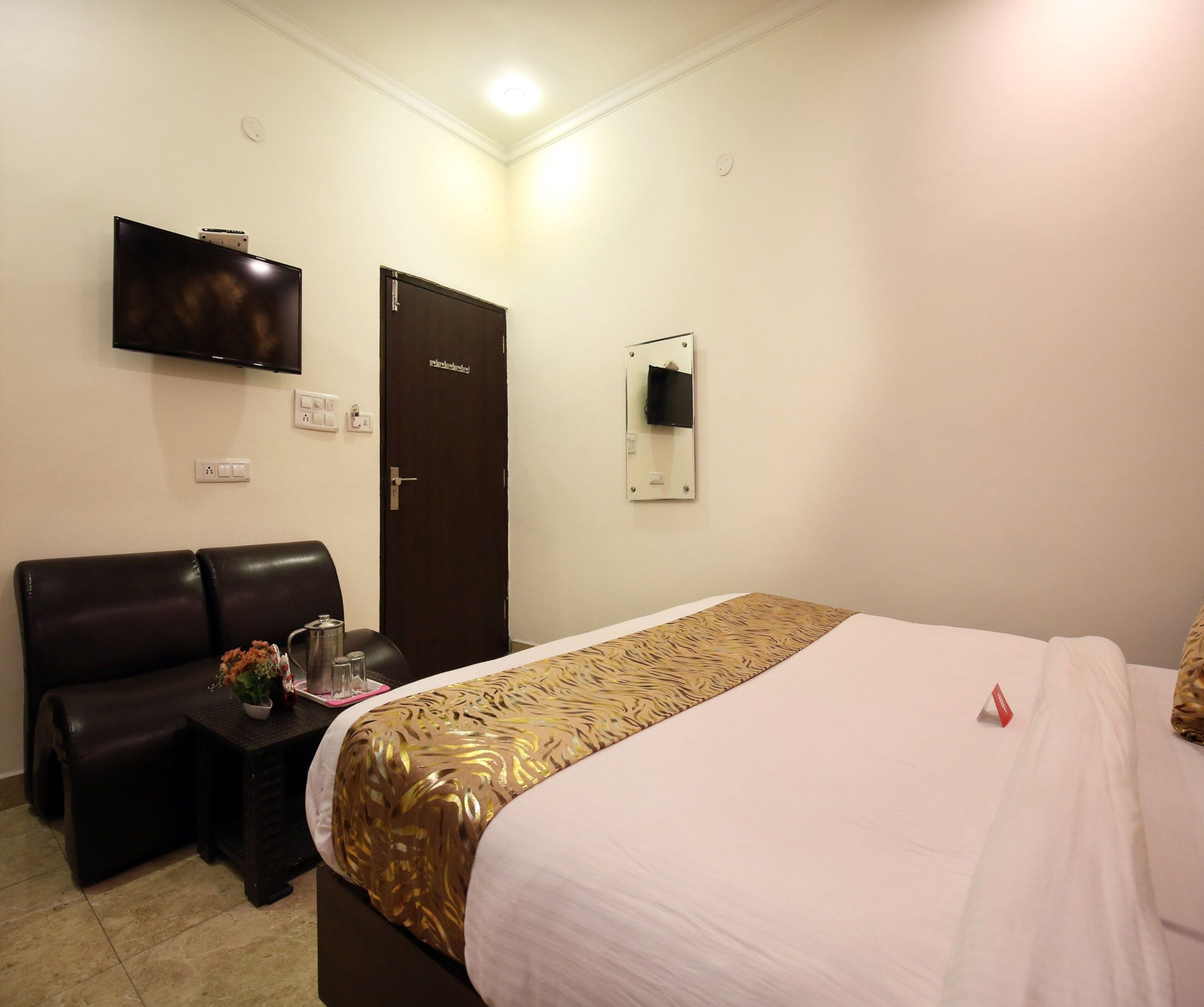 Une chambre d’hôtel comprenant un lit, un canapé, une petite table avec une carafe et des verres, un téléviseur à écran plat fixé au mur et une porte dotée d’un miroir.