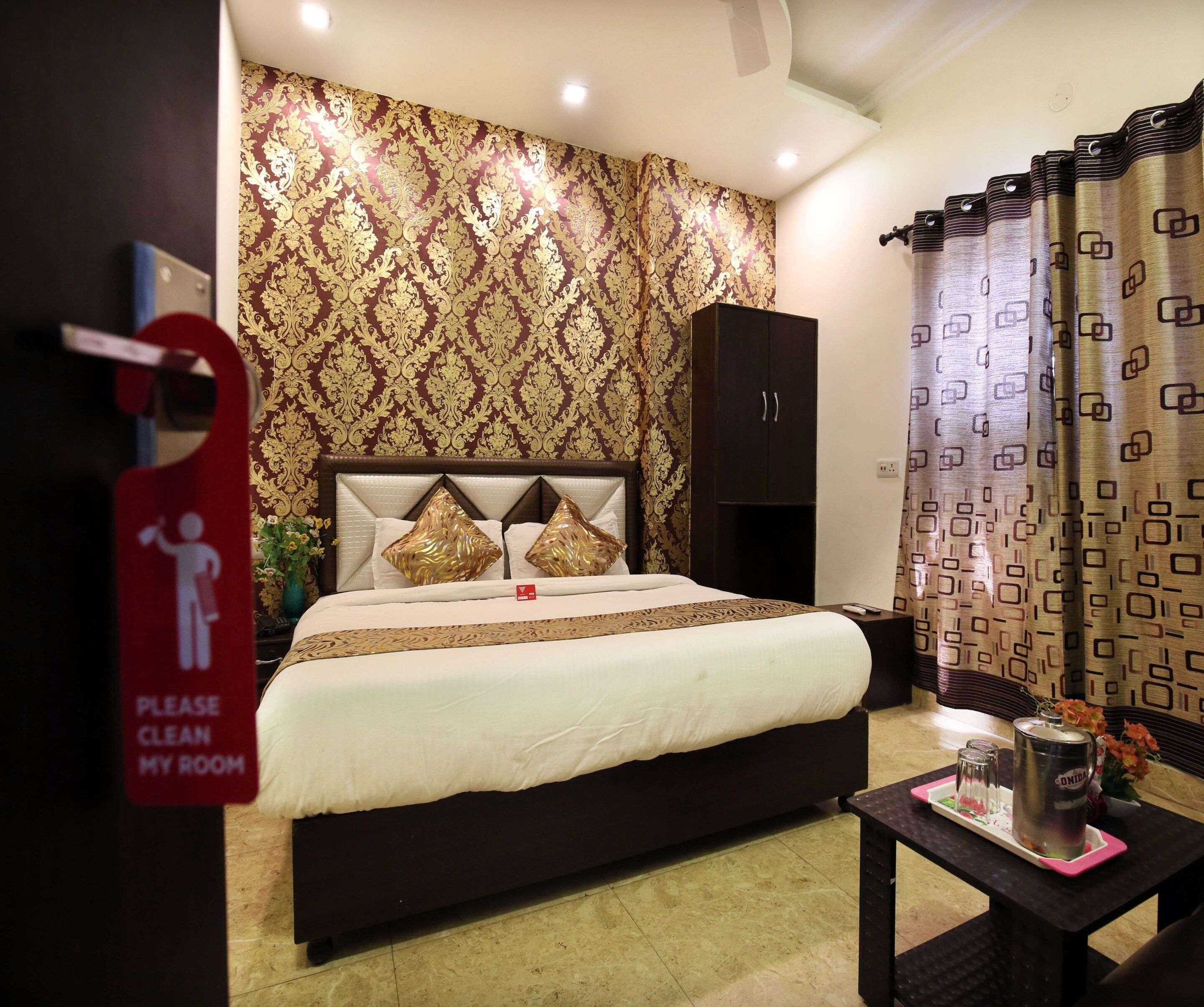 A hotel room with a bed, a nightstand, a cabinet, and a red sign on the door.