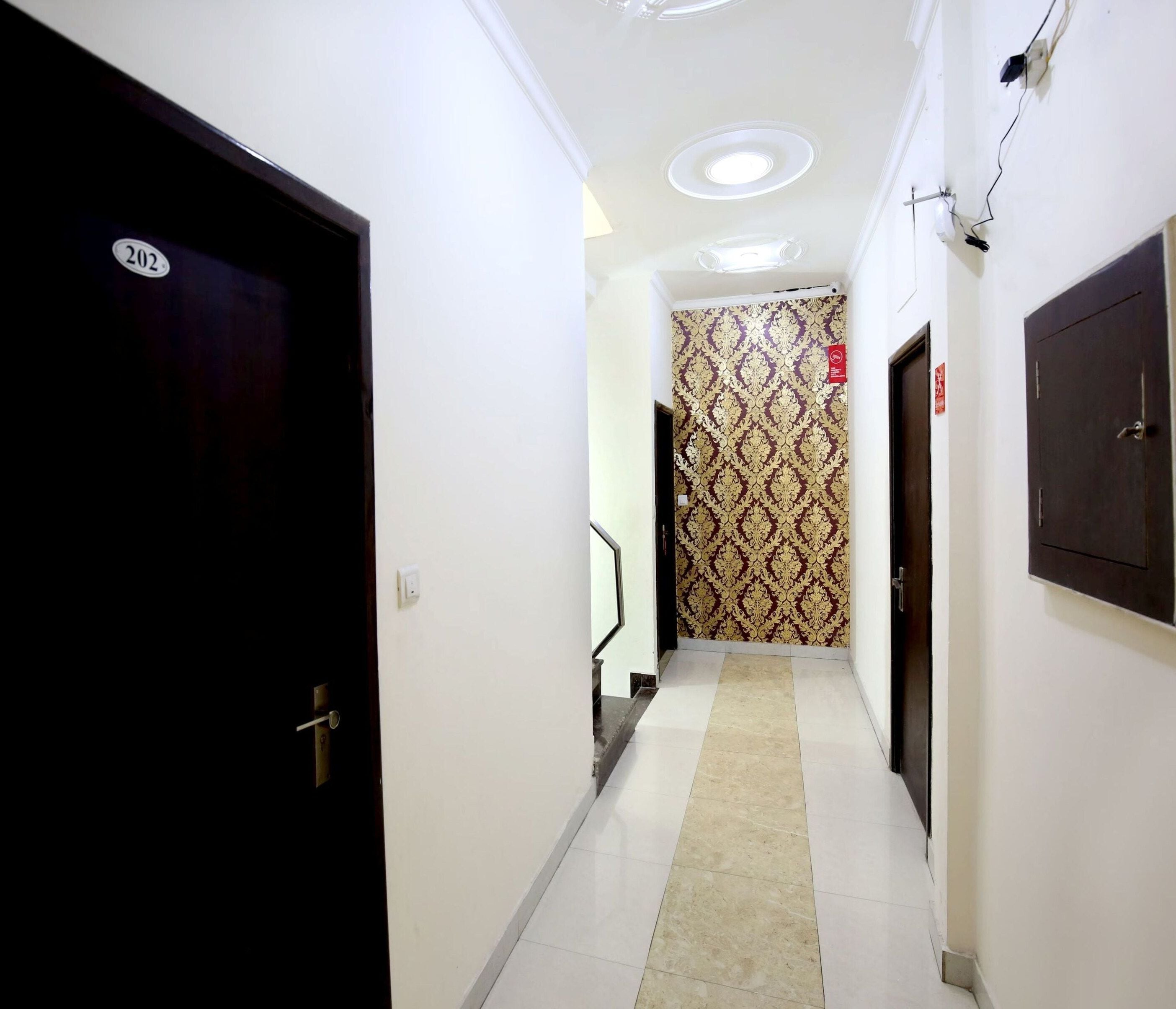 A hotel hallway with a black door on the left, a patterned wall in the center, and a dark door on the right.