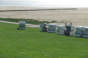 A grassy area with numbered containers, a path, and a beach in the background. - Lüdde Hus Mitteldiek (Nordstrand)