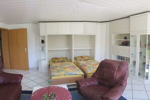 A room with two beds, a brown leather chair, a small round table, and a wardrobe with glass doors. - Holiday apartment with 2 bedrooms (Uhldingen-Mühlhofen)