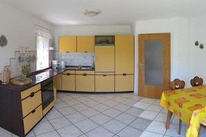 A compact kitchen with yellow cabinets, a built-in oven, and a dining area with a table covered in a yellow tablecloth. - Holiday apartment with 2 bedrooms (Uhldingen-Mühlhofen)