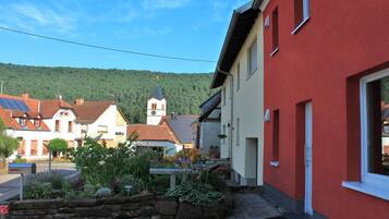 Ein rotes Gebäude mit einem Vorgarten aus Stein und eine Kirche im Hintergrund, dazu ein klarer Himmel.