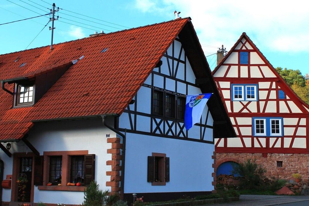 A traditional half-timbered house with a steep red-tiled roof and a blue flag.