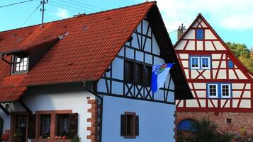 A traditional half-timbered house with a steep red-tiled roof and a blue flag.