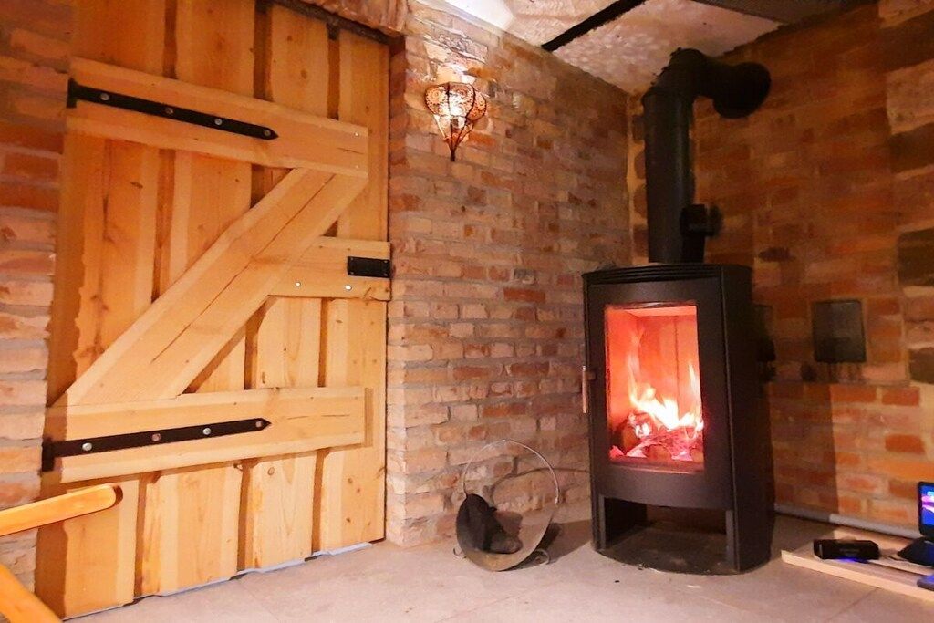 A room with a brick wall, a wooden door, and a wood-burning stove.