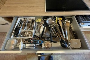Eine Schublade mit verschiedenen Küchenutensilien und Werkzeugen, darunter Löffel, Pfannenwender und ein Sieb.