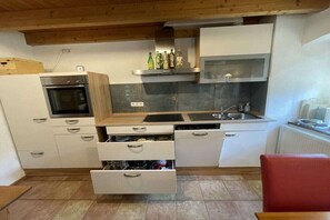 A compact kitchen with a built-in oven, a sink, and a countertop with bottles. - Backhaus Oberbettingen (Oberbettingen)