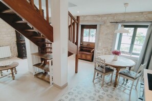 Ein Essbereich mit einem runden Tisch, Stühlen und einem Blumenstrauß. Eine Treppe mit Holzgeländern führt in einen anderen Raum.