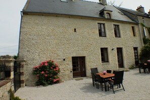 A stone building with a door, windows, and a small garden with pink flowers. - Holiday apartment with 2 bedrooms (Ste. Honorine des Pertes)