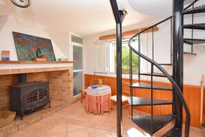 A spiral staircase in a room with a fireplace, a table with chairs, and a painting on the wall.