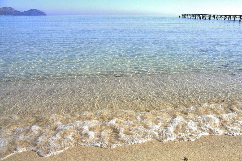 Una platja amb aigua cristal·lina, un tram de sorra i un moll que s'endinsa a la mar.